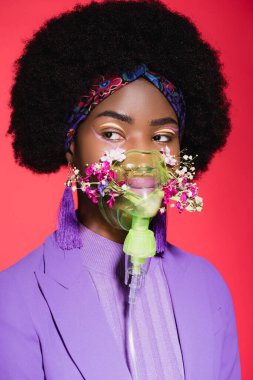 Afro-amerikan genç bayan mor renkli şık kıyafetli, solunum cihazında çiçekli, kırmızıda izole edilmiş.