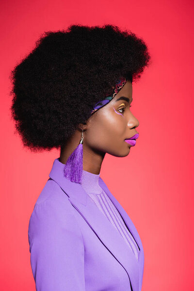 side view of african american young woman in purple stylish outfit isolated on red