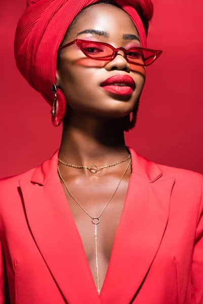 stock image african american young woman in stylish outfit, sunglasses and turban isolated on red