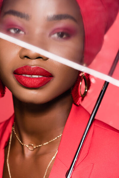 Африканская американская молодая женщина в стильном наряде и тюрбан держащий зонтик изолирован на красный