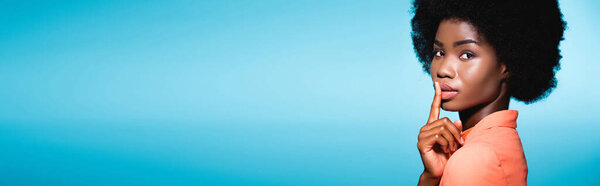 Африканский американец молодая женщина в оранжевом стильном наряде показывая Ш изолированы на синий, баннер