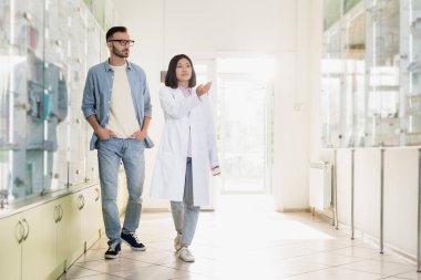 Eczanede müşteriyle yürürken beyaz önlüklü Asyalı eczacının elini göstermesi.