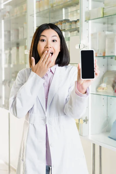 Excitado Asiático Farmacéutico Blanco Abrigo Cubierta Boca Mientras Celebración Smartphone —  Fotos de Stock