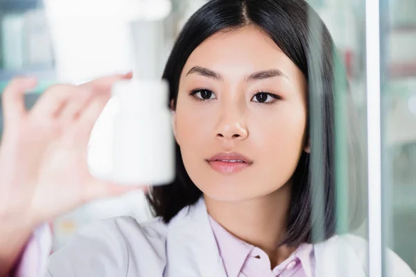 Asian Pharmacist White Coat Looking Bottle Blurred Foreground — Stock Photo, Image