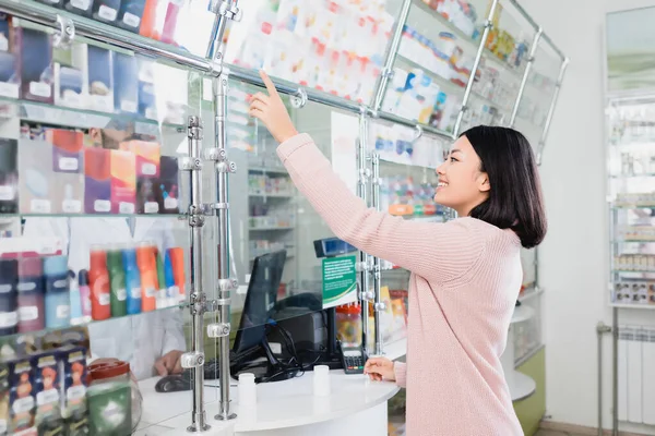 在药店里 快乐的亚洲顾客用手指指著接近卖家的药物 — 图库照片