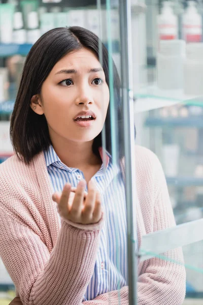 confused asian customer looking at bottle with medication on blurred foreground