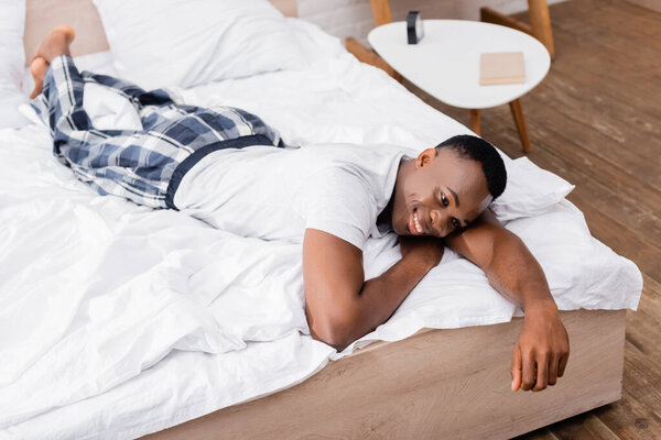 Smiling african american man in pajamas lying on bed during morning 