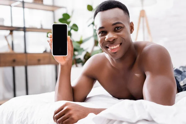 Hemdloser Afroamerikaner Zeigt Smartphone Mit Leerem Bildschirm Auf Dem Bett — Stockfoto