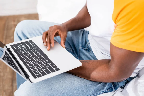 アフリカ系アメリカ人の男が朝にベッドに座っているときにノートパソコンを空の画面で使用しているのが見える — ストック写真