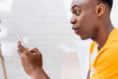 Evde akıllı telefon kullanan Afro-Amerikan bir adam şok oldu. 