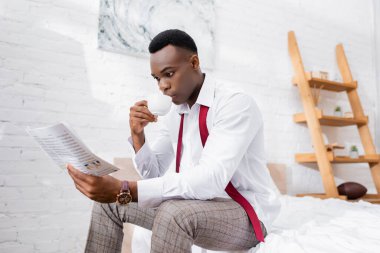 Afro-Amerikalı iş adamı kahve içiyor ve sabahları yatakta haber okuyor. 