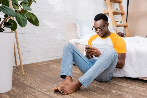 Hombre Afroamericano Descalzo Con Anteojos Usando Smartphone Piso Dormitorio — Foto de Stock