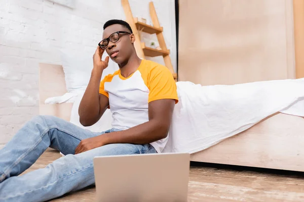 Tired African American Man Eyeglasses Sitting Laptop Blurred Foreground Bedroom — Stock Photo, Image