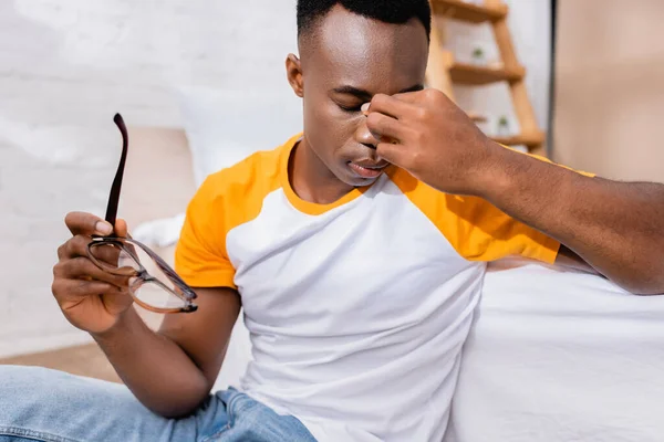 Hombre Afroamericano Cansado Sosteniendo Anteojos Cerca Cama — Foto de Stock