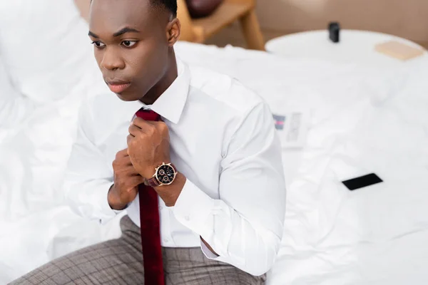 Africano Americano Empresário Ajustar Gravata Enquanto Sentado Cama Fundo Borrado — Fotografia de Stock
