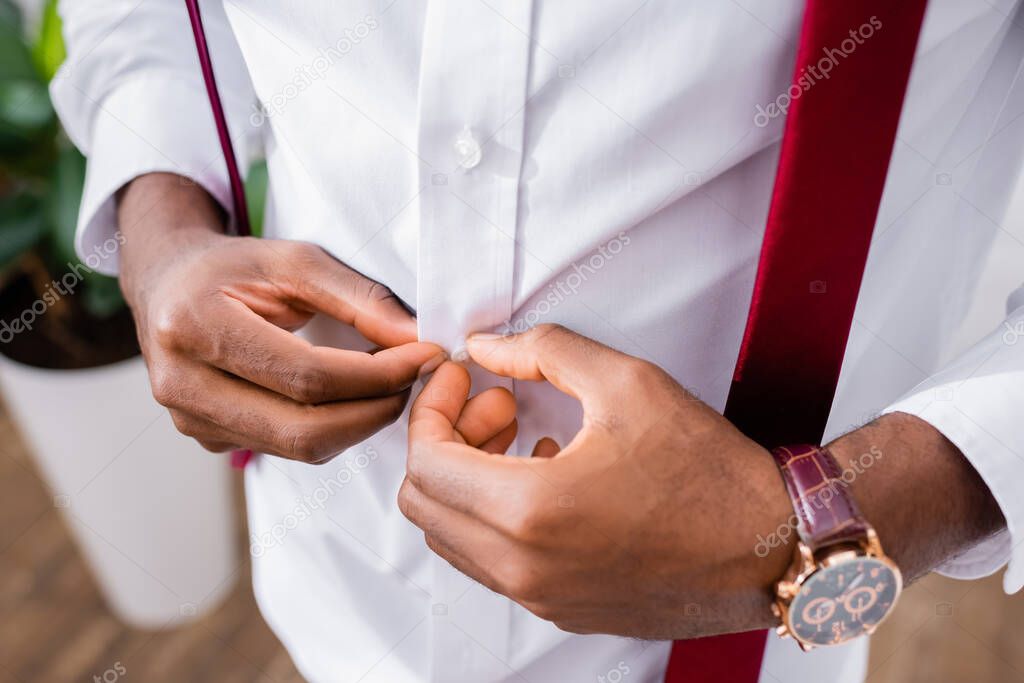 Cropped view of african american businessman buttoning shirt at home 