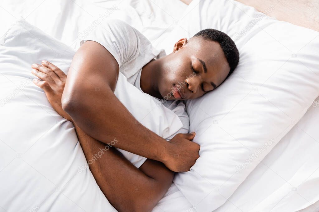 High angle view of african american man embracing pillow while sleeping at home 