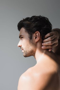 Boynuna yakın eli olan gömleksiz bir adam, gri üzerine izole bir şekilde bakıyor. 