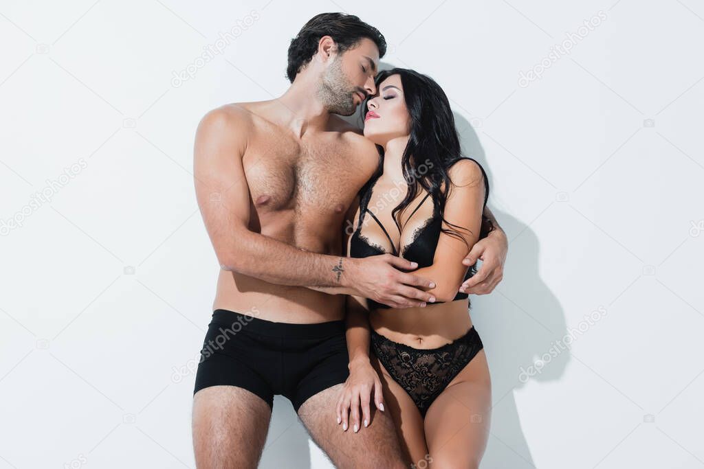 Shirtless man hugging girlfriend in lingerie with closed eyes on white background 