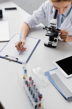 Laboratuvarda mikroskoba bakarken elinde kalem tutan bilim adamı