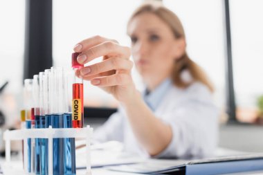 Numune ve bulanık arkaplan üzerinde doktorun elinde olduğu kovid harflerle test tüpü. 