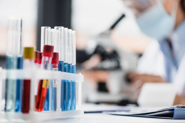 close up of glass test tubes with samples near doctor on blurred background
