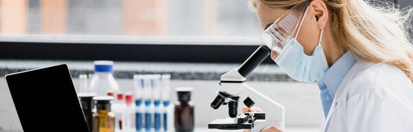 scientist in medical mask and goggles looking through microscope, banner