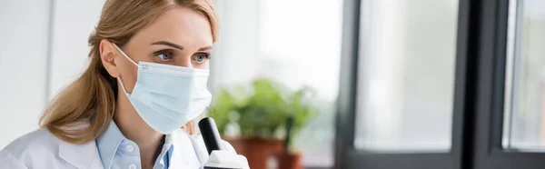 female scientist in medical mask looking away in lab, banner