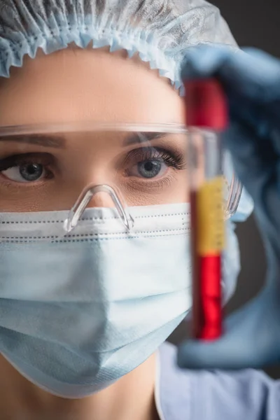 Tıbbi Şapkalı Maskeli Gözlüklü Hemşirenin Önplandaki Bulanık Test Tüpünü Tutarken — Stok fotoğraf