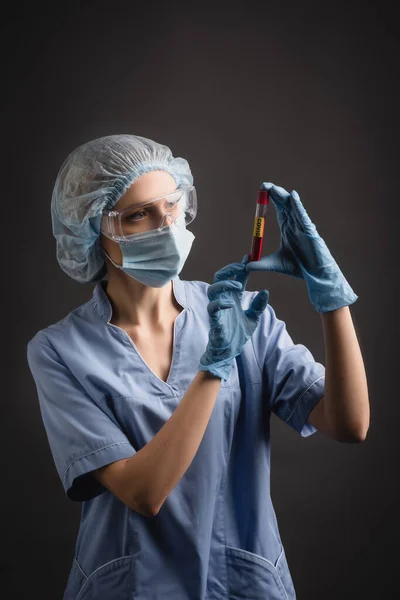 医療用キャップ マスク ゴーグルの看護師は暗い灰色で隔離された鮮やかな文字でテストチューブを見て — ストック写真