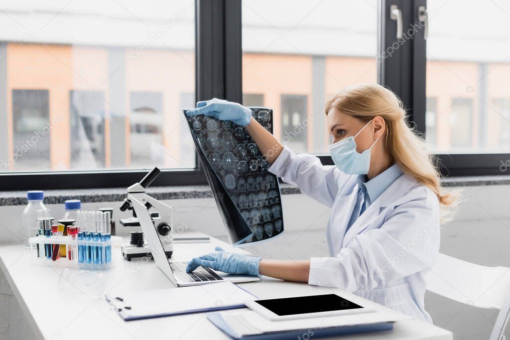 scientist in medical mask holding x-ray near devices on desk