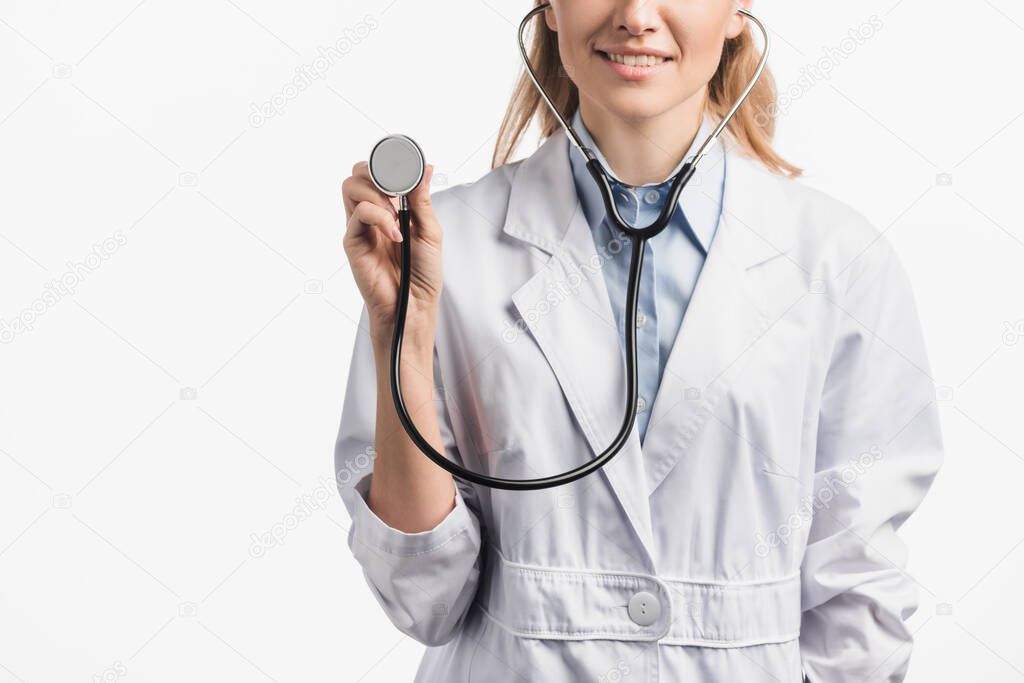 cropped view of happy nurse in white coat holding stethoscope isolated on white