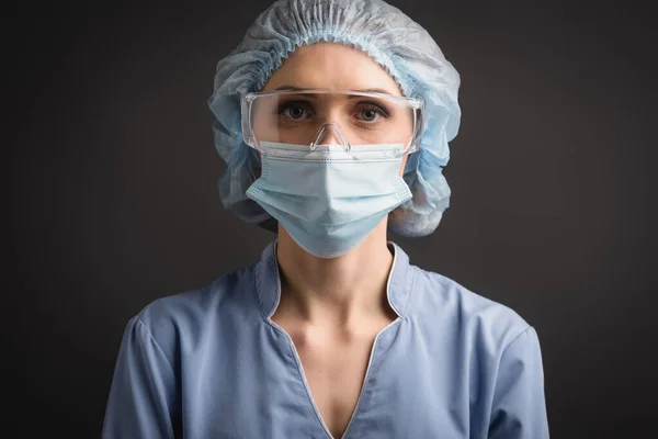 Pielęgniarka Czepku Medycznym Masce Goglach Patrząc Kamerę Odizolowaną Ciemnoszarym — Zdjęcie stockowe