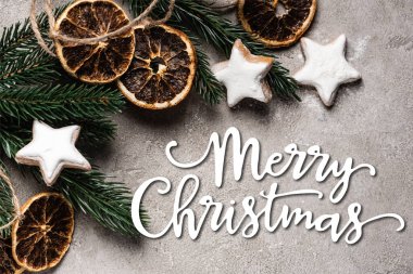Kurumuş portakal parçaları ve mutlu noel arkaplanda yazılı kurabiyelerle çam ağacının en üst görüntüsü.
