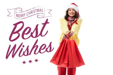 Noel Baba şapkası ve eşarplı neşeli genç bir kadın. Kırmızı alışveriş çantalarını Noel 'in yanında tutuyor. En iyi dileklerimle beyaz harflerle. 