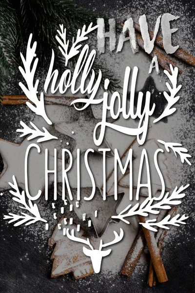 砂糖の粉とホリージョリークリスマスのレタリングで覆われた松の近くのジンジャーブレッドクッキーのトップビュー — ストック写真