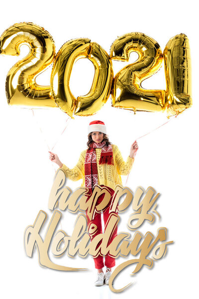 young woman in santa hat and scarf holding balloons with 2021 numbers near happy holidays lettering on white