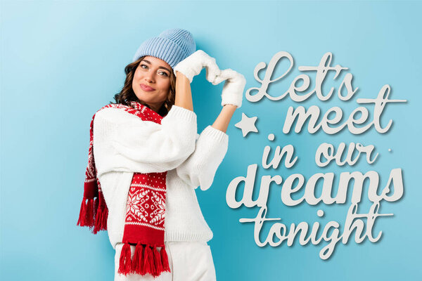 Радостная молодая женщина в теплом шарфе, перчатках и шляпе показывает знак сердца рядом Давайте встретимся в наших снах сегодня вечером буквы на синий