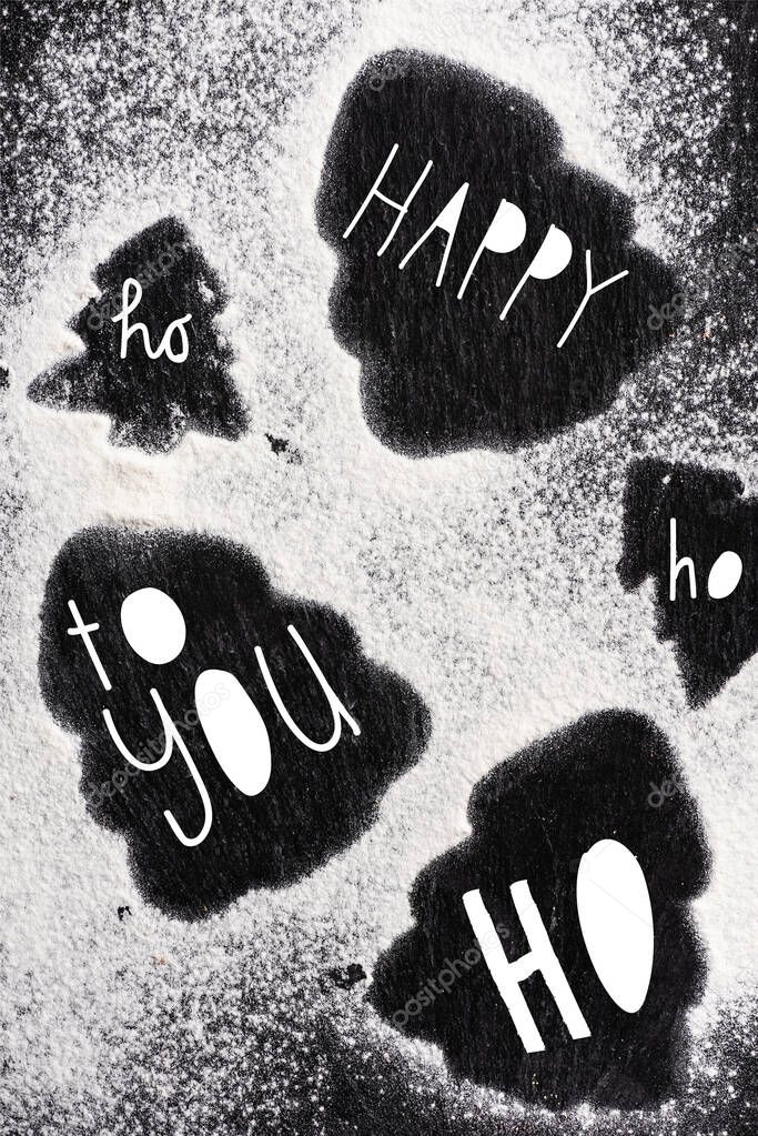 Top view of pine silhouettes covered with sugar powder with happy, ho ho ho, to you lettering 