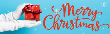 Eldivenli genç bir kadının, mutlu noel mektuplarının yanında, mavi pankartta hediye kutusu tutarken kısmi görüntüsü.