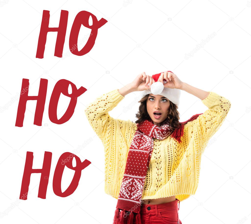 surprised young woman in scarf touching santa hat near ho ho ho lettering on white