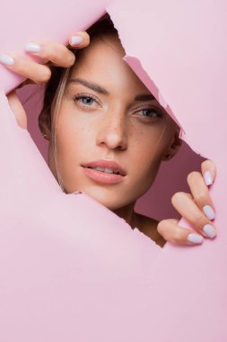 Pembe kağıt deliğinde çilli güzel bir kadın.