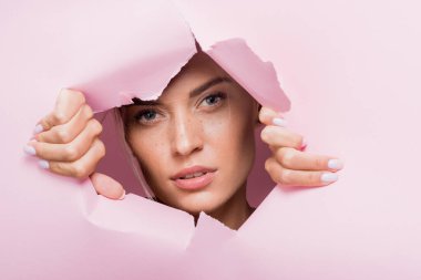 Pembe kağıt deliğinde çilli güzel bir kadın.