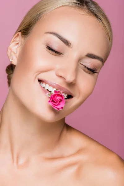 smiling beautiful woman with rose flower in mouth isolated on pink