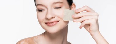 Gülümseyen, Vitiligo 'lu güzel bir kadın beyaz pankartta izole edilmiş gua sha kullanıyor.