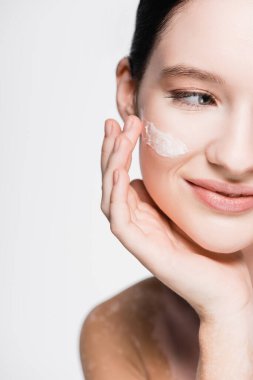 cropped view of smiling beautiful woman with vitiligo and facial cream on cheek isolated on white clipart