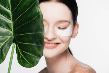 Gülümseyen genç ve güzel bir kadın vitiligo ve göz bantları ile yeşil yaprak yakınında beyaz izole