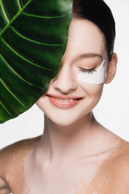Gülümseyen genç ve güzel bir kadın vitiligo ve göz bantları ile yeşil yaprak yakınında beyaz izole