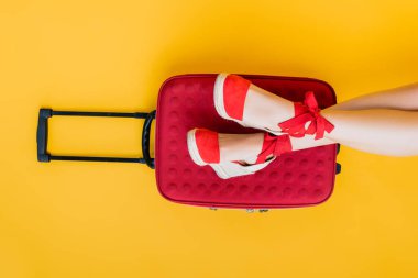 partial view of woman in wedge sandals near red suitcase on yellow  clipart