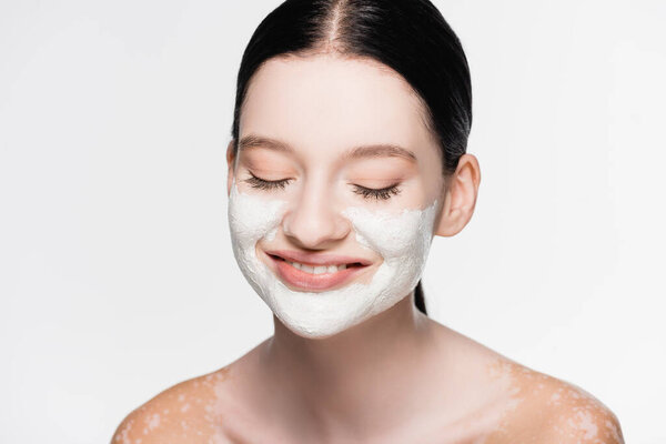 smiling young beautiful woman with vitiligo and clay mask on face isolated on white